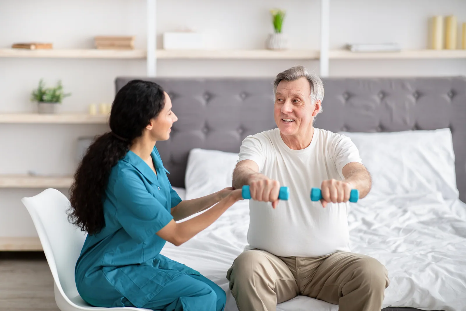A senior man working with dumbbells alongside a healthcare worker